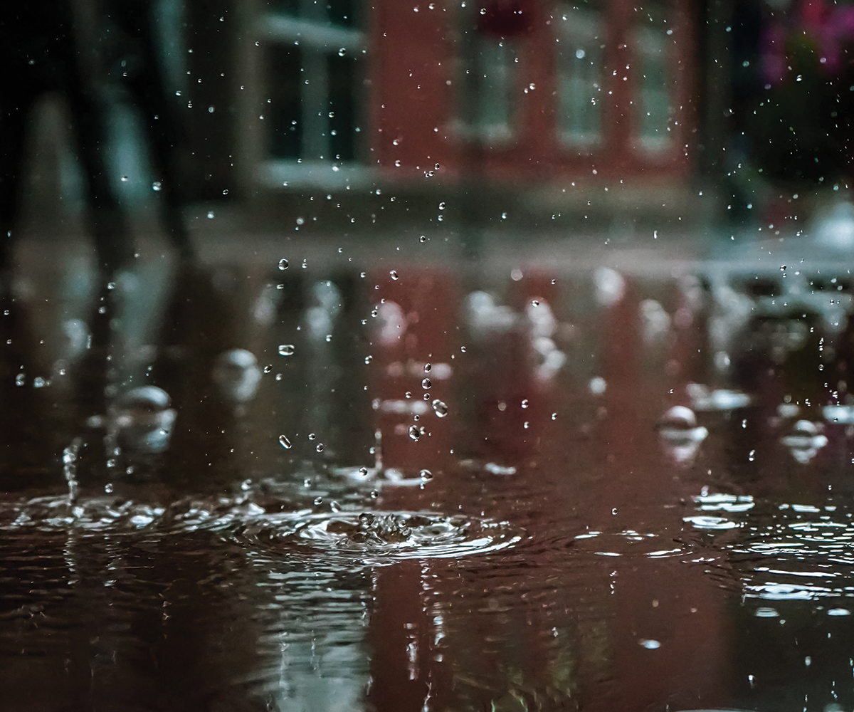 an out of focus background of buildings with raindrops falling into a puddle