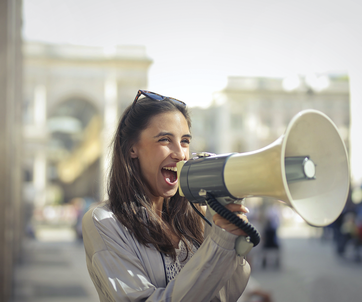 A lady is smiling and speaking into a megaphone